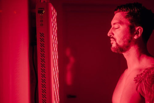 Man met gesloten ogen vlak bij een oplichtend rood licht paneel in een donkere kamer