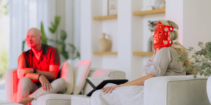 Twee personen op de bank, waarvan een het Liroma LED masker voor het gezicht draagt