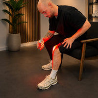 Man behandelt zittend zijn knie met de draagbare Liroma Portable Prime roodlichtlamp