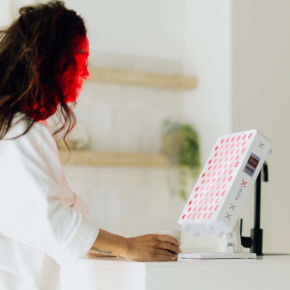 Vrouw behandelt haar gezicht bij het aanrecht met de Liroma Compact Gen5 roodlichtlamp